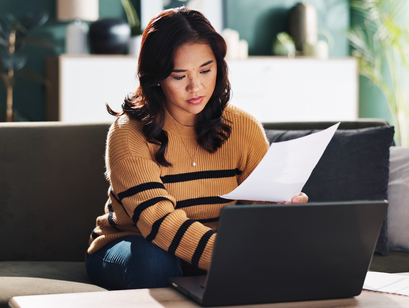 woman using laptop with paper in hand